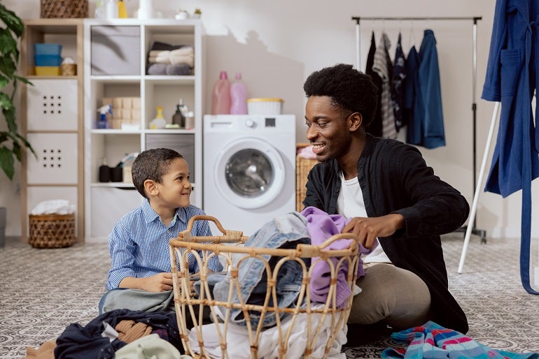 Young black son helping his dad with the laundry to prepare their clothes for drying