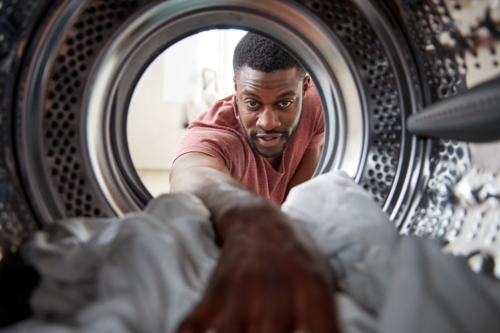 View from the inside of a tumble dryer with a young black man reaching inside to take clothes out of the machine