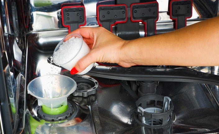 Cropped shot of a female hand pouring dishwasher salt in to a dishwasher to soften the water