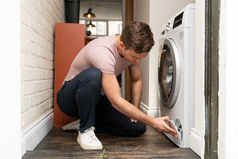 Young blonde Caucasian man carrying out washing machine maintenance