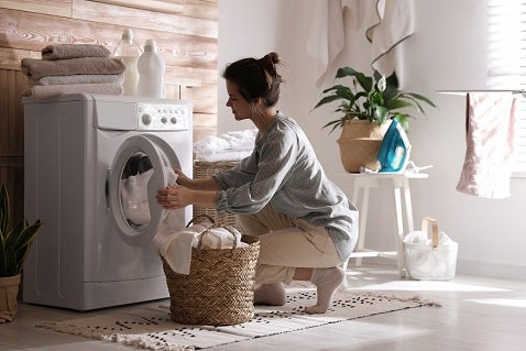 Young brunette Caucasian woman kneeling down to take the laundry out of the washing machine at home