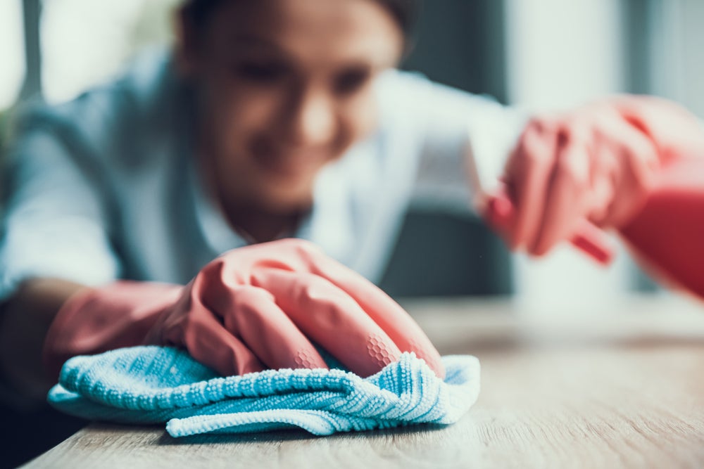 Cropped shot of a female wearing pink rubber gloves to clean the table with a blue microfibre cloth