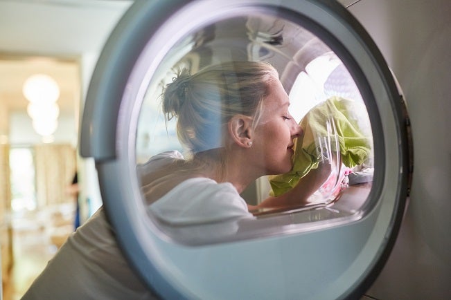 Young blonde Caucasian housewife sniffing fresh laundry that's just finished being tumble dried